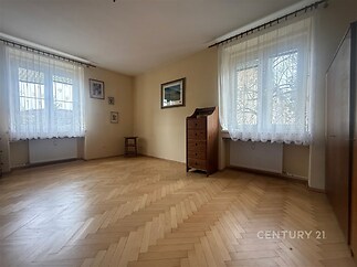 Světlý obývací pokoj s parketovou podlahou, velká okna, minimalistický design, vhodný pro moderní bydlení.