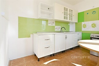 Světlá kuchyň s dlažbou, bílými skříňkami a zelenými obklady, moderní design, velká okna poskytují dostatek přirozeného světla.