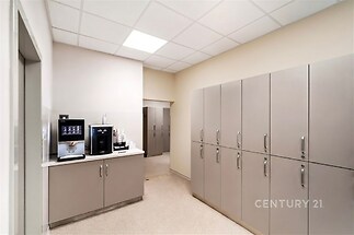 Moderní kancelářská kuchyňka, světlá s vestavěnými skříněmi, laminátová podlaha, vybavená automatickým kávovarem, ideální pro pracovní prostředí.