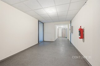 Chodba s dlažbou, bílými stěnami a moderním osvětlením poskytuje prostorný a udržovaný prostor v obytné budově.