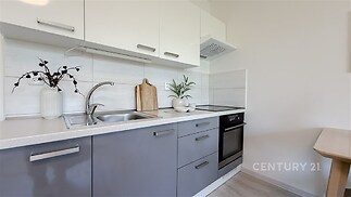 Moderní kuchyň s vestavěnou troubou a světlými skříňkami, dřevěný dekor a dlažba na stěně, světlé a čisté provedení.