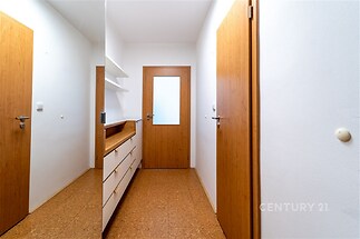 Úzká vstupní chodba s korkovou podlahou a dřevěnými dveřmi, vybavená vestavěnými skříněmi pro úložný prostor.