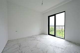 Světlá ložnice s dlažbou a velkým oknem, které poskytuje výhled do zahrady, moderní minimalistický design bez nábytku.