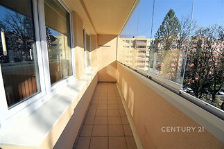 Zasklený balkon s dlažbou a velkými okny nabízí výhled na klidnou ulici. Světlý prostor je ideální pro relaxaci a užívání si slunečních dnů.