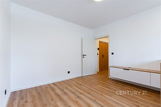 Světlý obývací pokoj s parketovou podlahou, moderní úložnou skříní a bílými stěnami, ideální pro stylové bydlení.