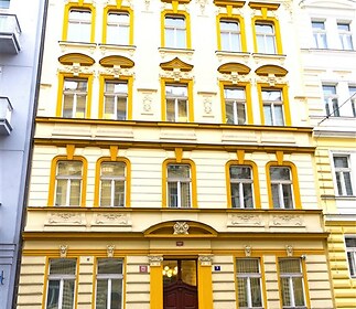 Historická fasáda s okny zdobenými štukovými detaily, renovovaný městský dům v centru. Skvělá lokalita a architektonický styl.