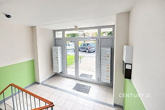 Vstupní hala panelového domu, dlažba, poštovní schránky, moderní dveře, bezpečnostní kamera, světlé stěny, dobře udržovaná.