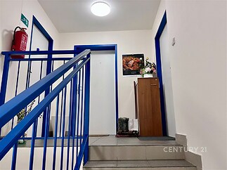 Chodba bytového domu s dlažbou, modrým zábradlím a bílými stěnami, čistý a údržbovaný prostor, ideální pro klidné bydlení