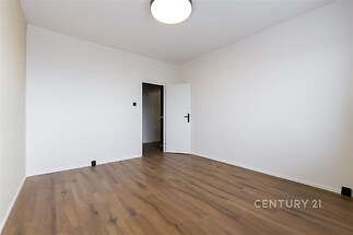 Prázdná ložnice s dřevěnou podlahou, světlé stěny a moderní osvětlení, připravená k úpravě dle vlastního vkusu.