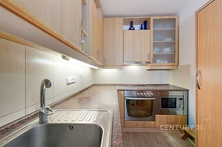 Kompaktní kuchyň s dřevěnými skříňkami, moderními spotřebiči a dlažbou. Vhodné pro efektivní vaření a úložné prostory.