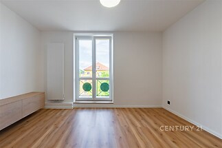 Světlý obývací pokoj s parketovou podlahou, velká okna a moderní minimalistický design, vytváří světlou a příjemnou atmosféru.
