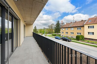Prostorný balkon s moderní dlažbou, kovovým zábradlím a velkými okny nabízí svěží výhled na poklidnou rezidenční ulici.