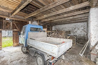 Prostorná garáž s dřevěným stropem, kamennými zdmi a velkými vraty, ideální pro skladování nebo dílnu, s parketovou podlahou.
