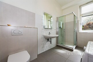 Koupelna s moderní sprchou, dlažbou a velkým oknem zajišťujícím dostatek světla, v kombinaci světlých dlaždic a bílých stěn.