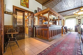 Prostorný interiér s dřevěným barem, dlažbou na podlaze a dekorativním dřevěným stropem, ideální pro podnikání nebo společenské akce.
