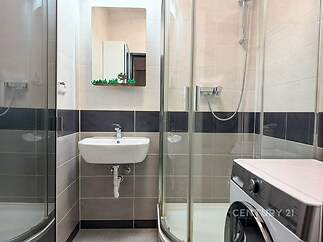Koupelna s moderním sprchovým koutem, světlými obklady a pračkou.