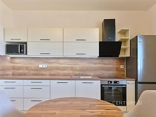 Moderní kuchyň s dřevěnou pracovní deskou, vestavěnými spotřebiči a světlými skříňkami vytváří elegantní a funkční prostor.