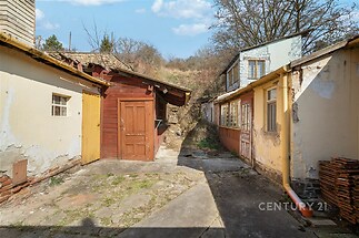 Malebný dvorek s venkovskou atmosférou nabízí mix dlažby a kamenných cest, obklopený klasickými přístavbami s dřevěnými dveřmi a rustikální střešní krytinou.