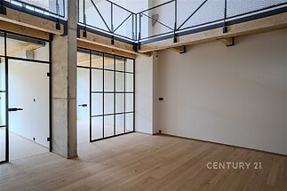 Prostorný obývací pokoj s parketovou podlahou, moderní skleněné dveře a ocelové prvky, světlý interiér s vysokým stropem.