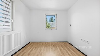 Prázdná místnost s parketovou podlahou, bílými stěnami a velkým oknem. Světlé prostory ideální pro moderní styl bydlení.