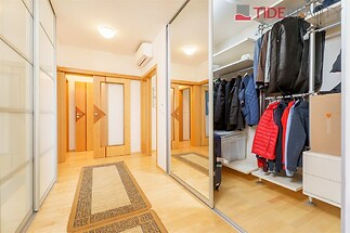 Prostorná chodba, dřevěná podlaha, vestavěné skříně, moderní interiér, světlá stěna, elegantní úložné řešení.