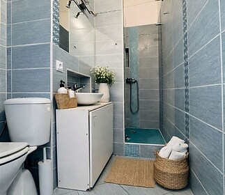 Moderní koupelna s dlažbou a sprchovým koutem, světlé stěny doplněné o stylové mozaikové prvky, čistý a udržovaný prostor.