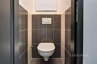 Koupelna s moderními keramickými dlaždicemi, závěsnou toaletou a čistým designem. Minimalistický styl dodává prostoru elegantní vzhled.