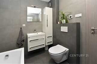 Moderní koupelna s dlažbou, bílou závěsnou toaletou a elegantními skříňkami. Minimalistický design a světlé povrchy dodávají prostoru čistotu.