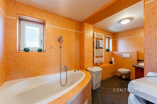 Koupelna s dlažbou, rohovou vanou a moderním vybavením, světlá díky velkému oknu, obsahuje topný žebřík a kvalitní keramiku.