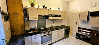 Moderní kuchyň s dlažbou, světlá dřevěná kuchyňská linka, vestavěná trouba, plynový sporák, nerezový dřez, dekorativní police, stěna s noži.