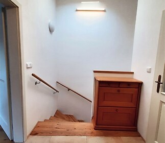 Světlé schodiště s parketovou podlahou, dřevěné zábradlí, moderní osvětlení a vestavěná skříňka, přirozené světlo díky střešnímu oknu.