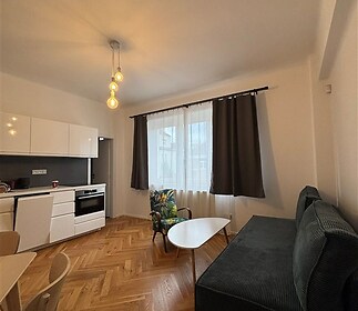 Moderní obývací pokoj s parketovou podlahou, velkými okny a světlým interiérem, ideální pro pohodlné bydlení v rekonstruovaném prostoru.