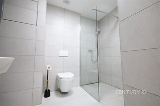 Moderní koupelna s velkoformátovou dlažbou, sprchovým koutem a závěsnou toaletou, čisté linie a minimalistický design.