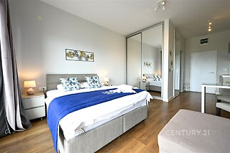 Prostorná ložnice s parketovou podlahou, vestavěné skříně, moderní styl, světlé textilie a elegantní osvětlení, ideální pro pohodlný odpočinek.