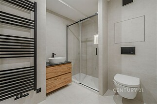 Moderní koupelna s keramickou dlažbou, skleněným sprchovým koutem a dřevěným umyvadlovým stolem, stylové interiérové prvky.