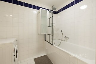 Koupelna s bílými dlaždicemi, moderní sprchovou hlavicí a vanou, která zajišťuje světlý a čistý vzhled, ideální pro relaxaci.