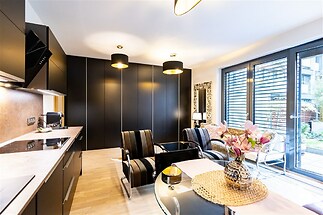 Moderní obývací pokoj s parketovou podlahou, velkými okny a elegantním černým nábytkem, ideální pro světlé a stylové bydlení.