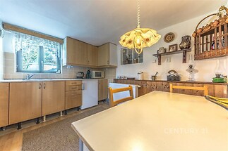 Kuchyň se světlou dřevěnou linkou, parketovou podlahou a velkým oknem, které zajišťuje dostatek přirozeného světla, v rustikálním stylu.