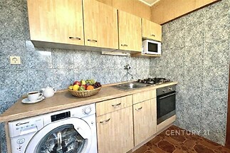 Kompaktní kuchyň s dřevěnými skříňkami, dlažbou a vestavěnými spotřebiči. Obsahuje pračku a malou mikrovlnnou troubu.