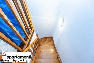 Dřevěné schodiště s parketovou podlahou a moderním osvětlením, doplněné o čistě bílé stěny, vytváří světlý a útulný prostor.