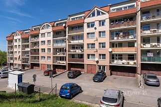 Pohled na bytový dům s balkony, parkovištěm a moderní fasádou. Budova je světlá a dobře udržovaná, ideální pro městské bydlení.