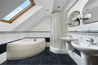 Moderní koupelna s černou dlažbou, rohovou vanou a sprchovým koutem, vybavená dvěma umyvadly a vestavěným střešním oknem pro světlý interiér.