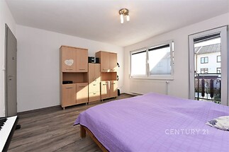 Prostorná ložnice s laminátovou podlahou, moderní vestavěné skříně a velká okna s výhledem na terasu, světlý a vzdušný interiér.