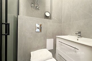 Moderní koupelna s šedými dlaždicemi, elegantním umyvadlem a úložným prostorem, sprchový kout s moderními armaturami, čistý a světlý design.
