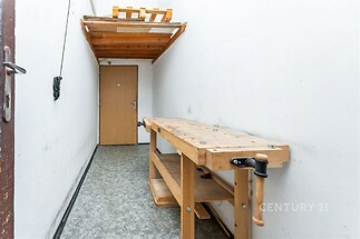 Úložný prostor s dřevěným pracovním stolem, betonová podlaha, regály, vhodný pro dílnu nebo skladovací účely, v dobrém stavu.
