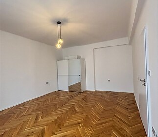 Světlá ložnice s parketovou podlahou a moderním osvětlením, nabízí vestavěné skříně a minimalistický design ve světlých odstínech.