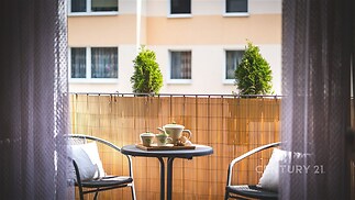 Balkon s dřevěným plotem a venkovním posezením, výhled na bytovou zástavbu, moderní styl, ideální pro relaxaci a odpočinek.
