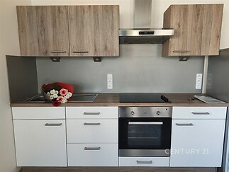 Moderní kuchyň s dřevěnými skříňkami, vestavěnou troubou a skleněným obkladem, vybavená varnou deskou a digestoří.
