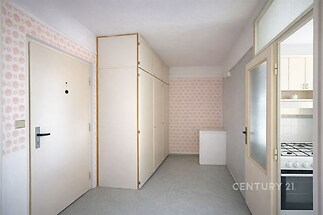 Předsíň s vestavěnými skříněmi, světle růžová tapeta, vinylová podlaha, světlé dveře vedoucí do kuchyně, moderní styl, dobře udržovaný stav.