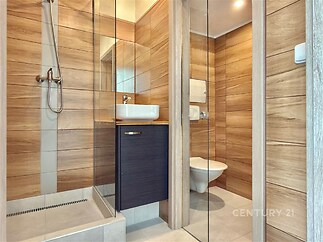 Moderní koupelna s dřevěným obkladem, skleněným sprchovým koutem a závěsnou toaletou, vkusný a elegantní design.
